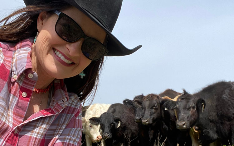 Women wearing black cowboy hat posing with cattle.